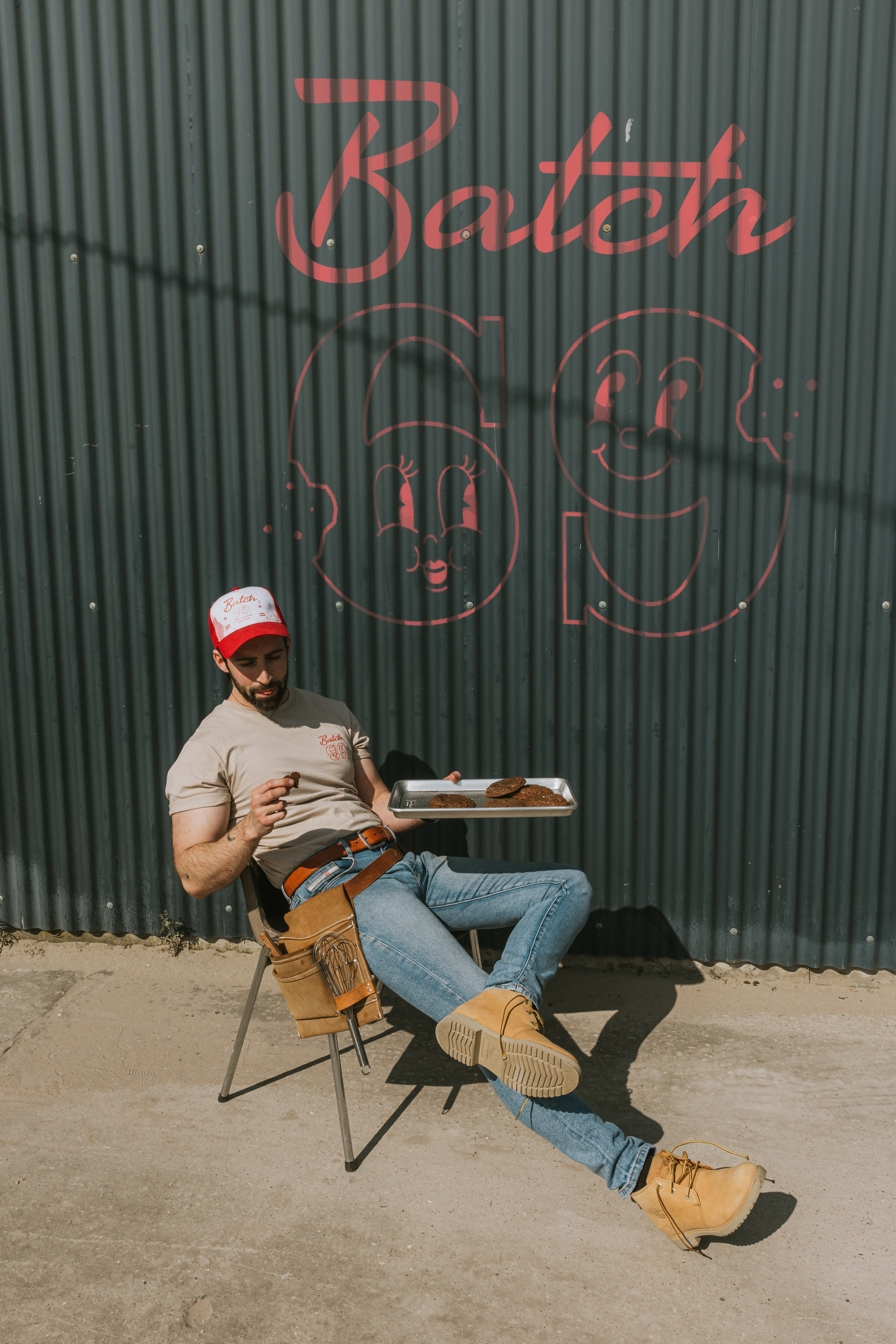 Batch69 founder relaxing in front of the brand mural painted on a corrugated green industrial wall in Bruges